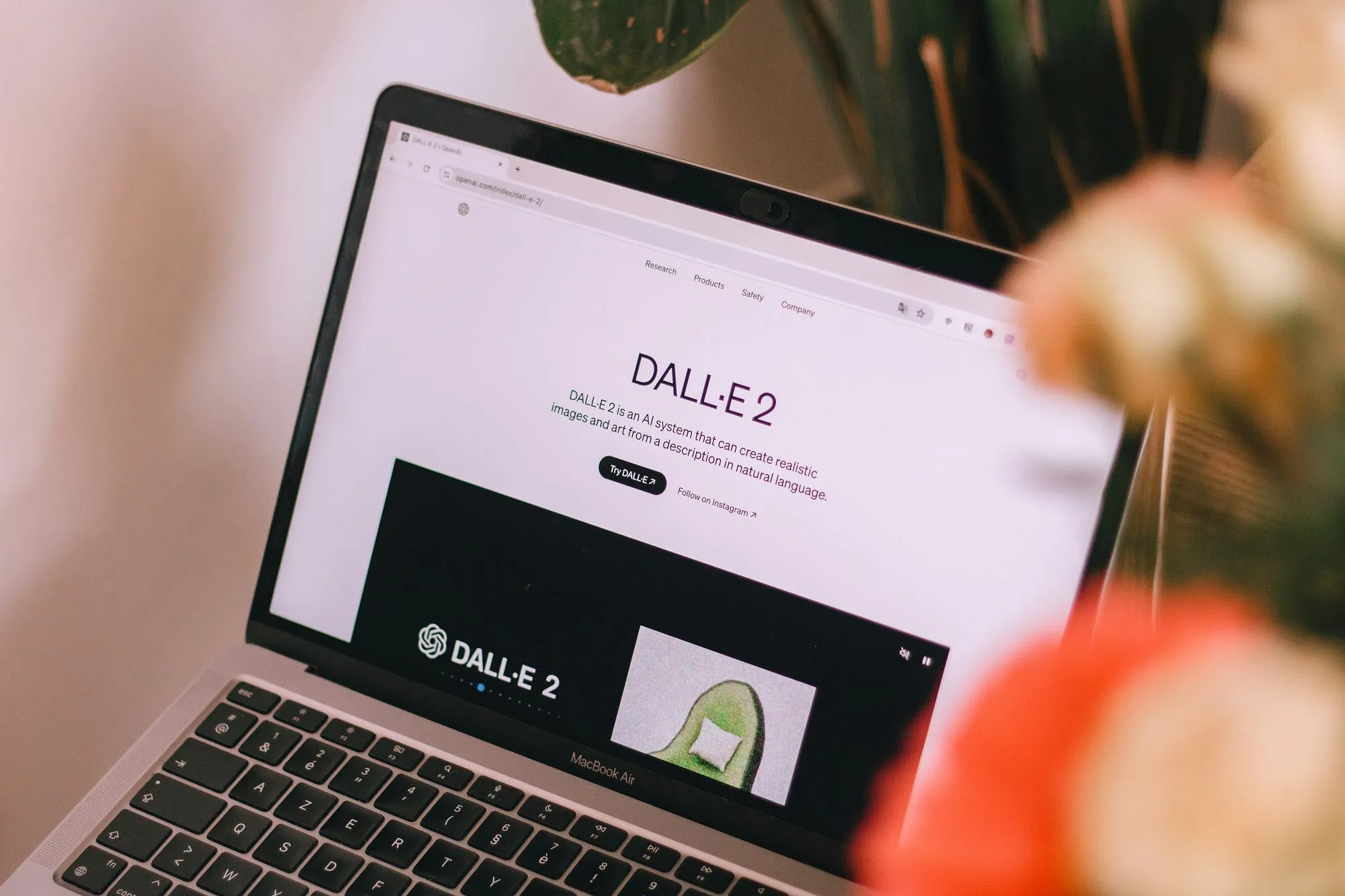 A laptop on a desk showing the DALL-E 2 landing page, beside a vase of flowers.