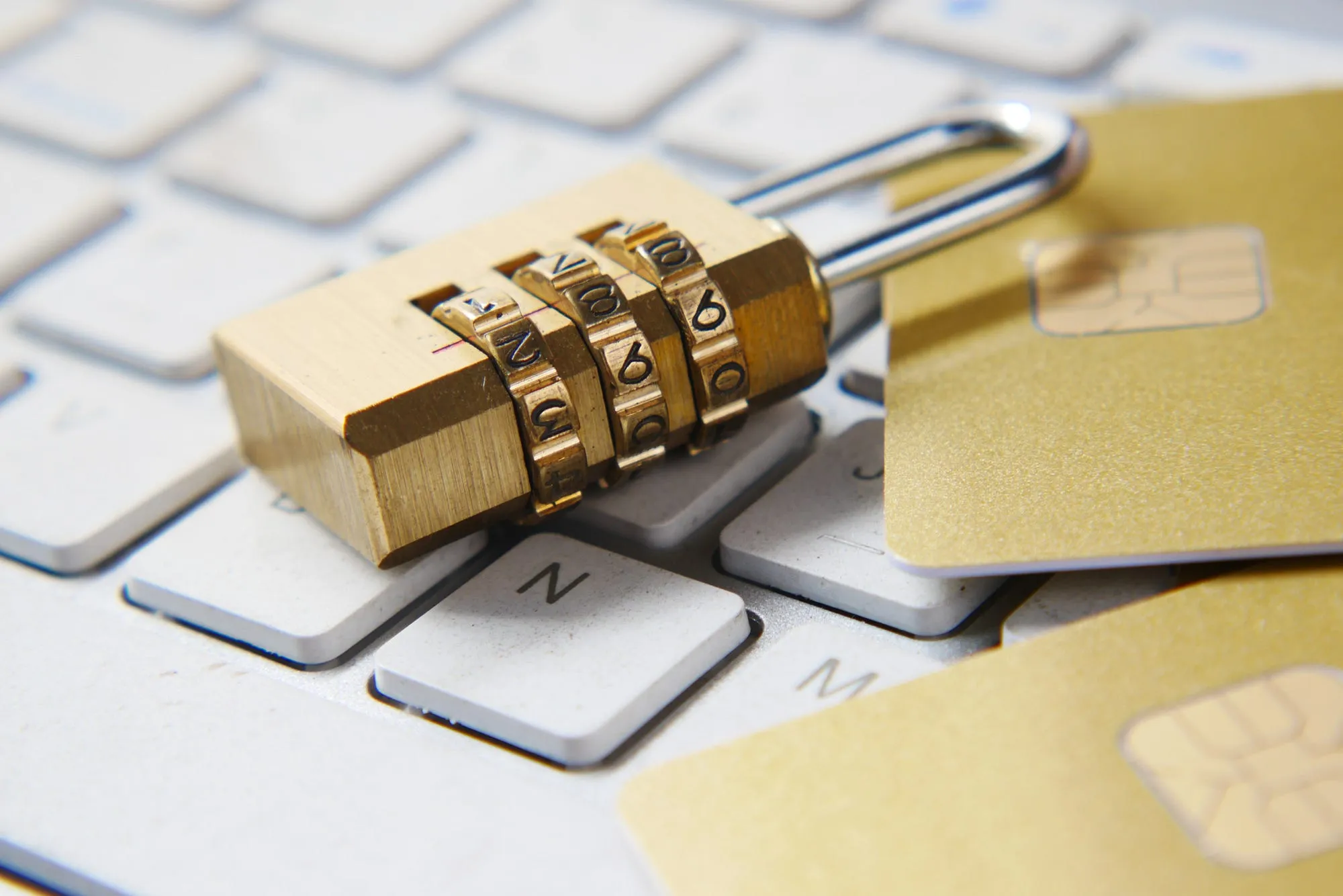 A combination padlock resting on a white keyboard next to two gold credit cards.